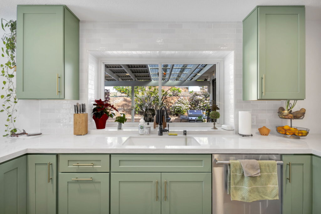 Sage green kitchen cabinets with white countertops and garden window in San Diego