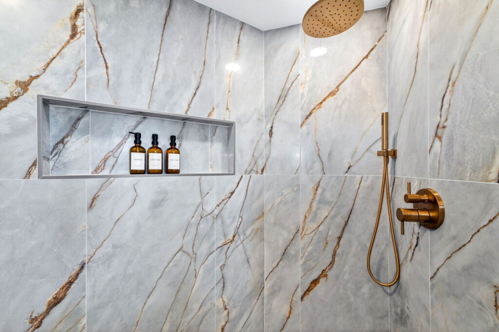 Custom marble shower with built-in niche and gold fixtures by PBH Builders